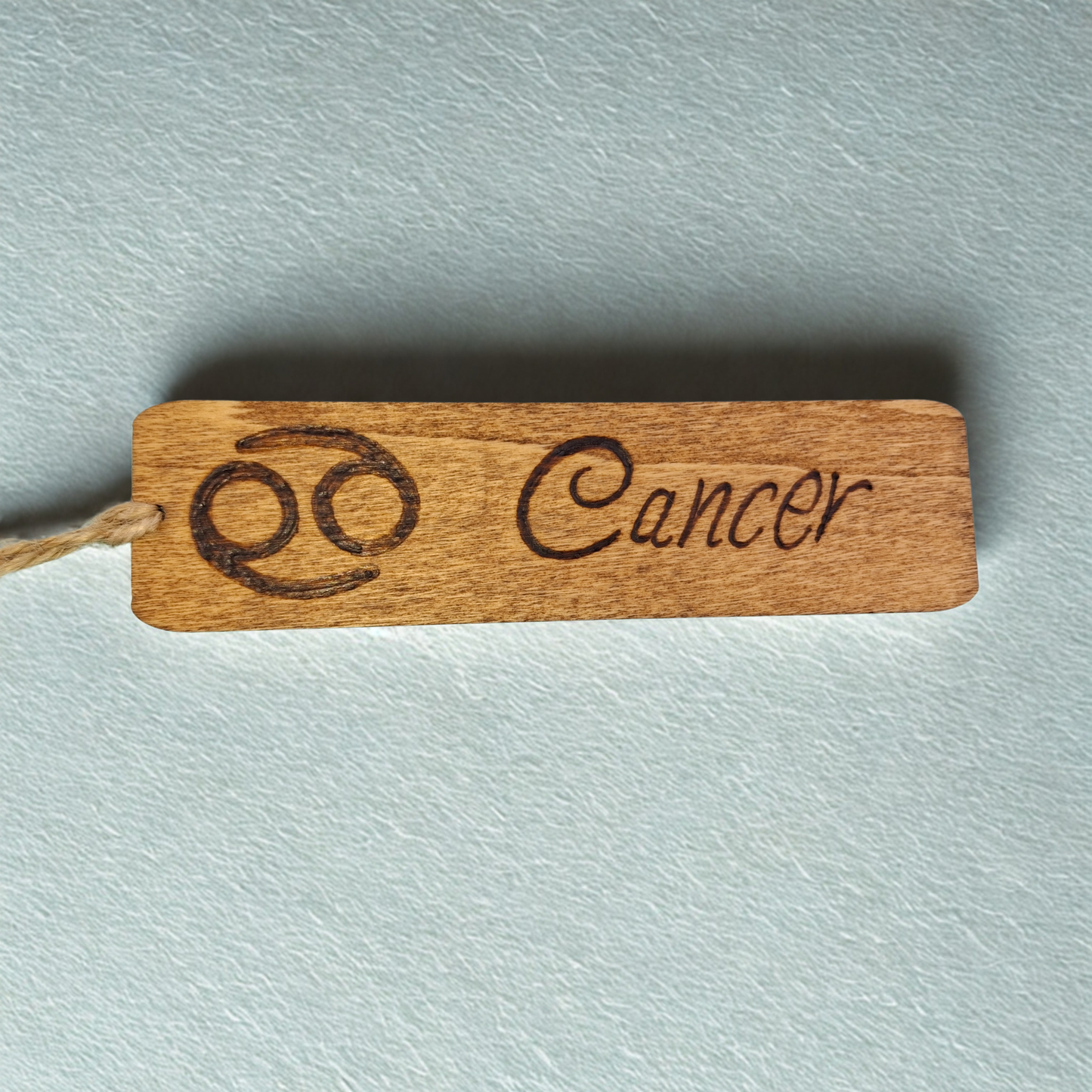 Dark wood bookmark with "Cancer" pyrography and a star sign illustration.