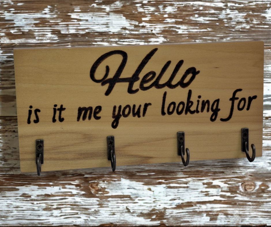 A four-hook hanger crafted from two-tone Tulipwood, featuring hand-burnt lettering that reads "Hello, Is It Me You're Looking For?" The wood has visible grain, showcasing its natural variations.