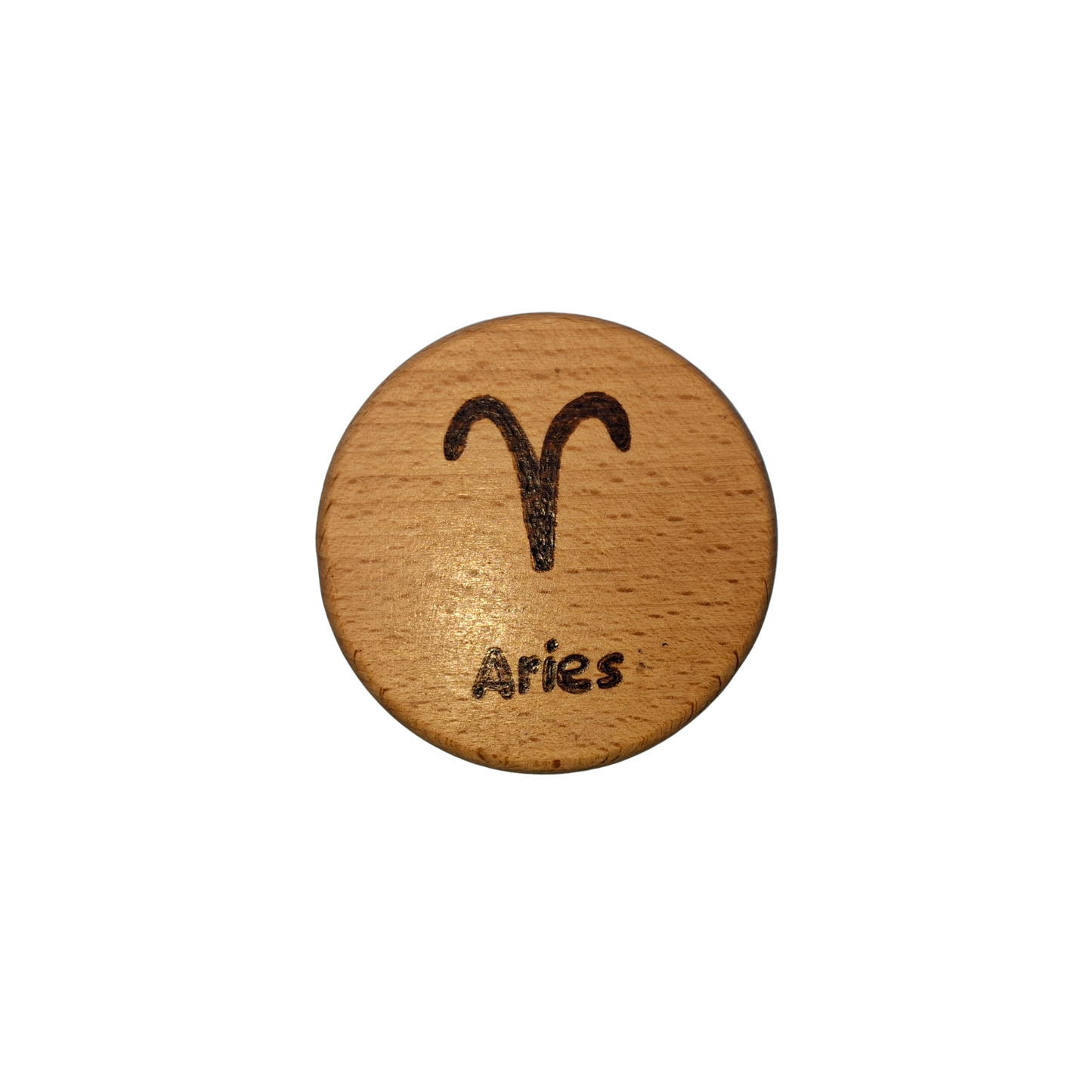 Close-up of a light-colored beechwood circle, 5cm in diameter and 0.4cm thick, featuring the words "Aries" and an illustration of the star sign symbol, hand-burned into its surface using pyrography. The wood has a smooth, waxed finish and the text is clearly legible.