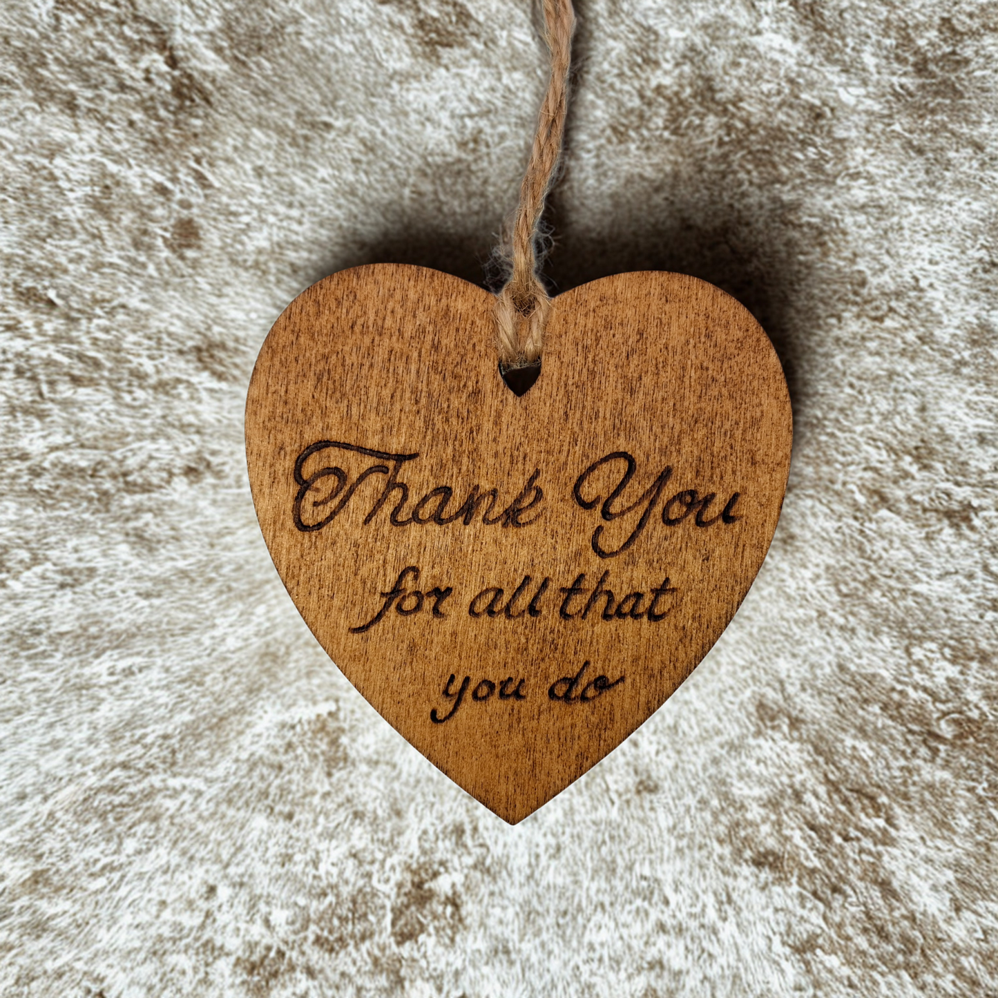 Heart-shaped wooden ornament, hand-drawn with pyrography, featuring the engraved phrase "Thank you for all that you do" in a decorative script, set against a textured background.