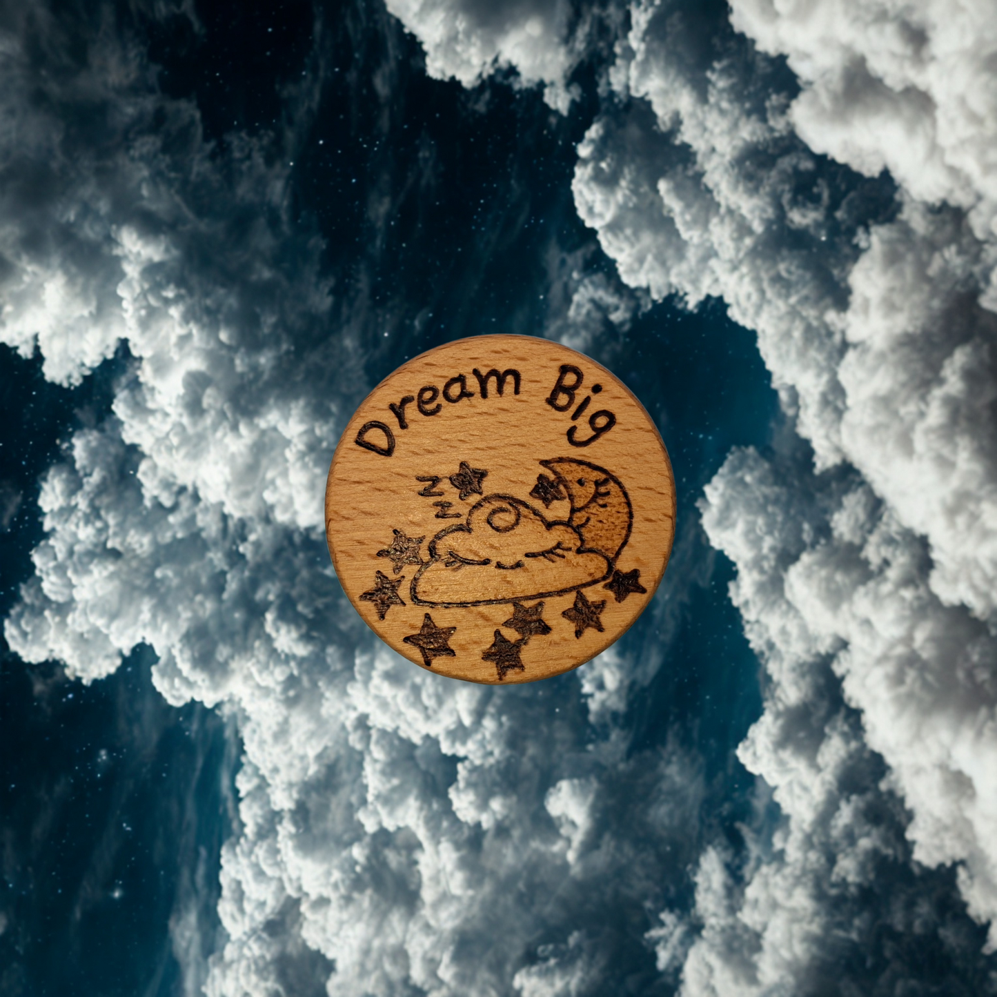 Close-up of a light-colored beechwood circle, 5cm in diameter and 0.4cm thick, featuring the words "Dream Big" and an illustration of a sleeping cloud, moon and stars hand-burned into its surface using pyrography. The wood has a smooth, waxed finish and the text is clearly legible.