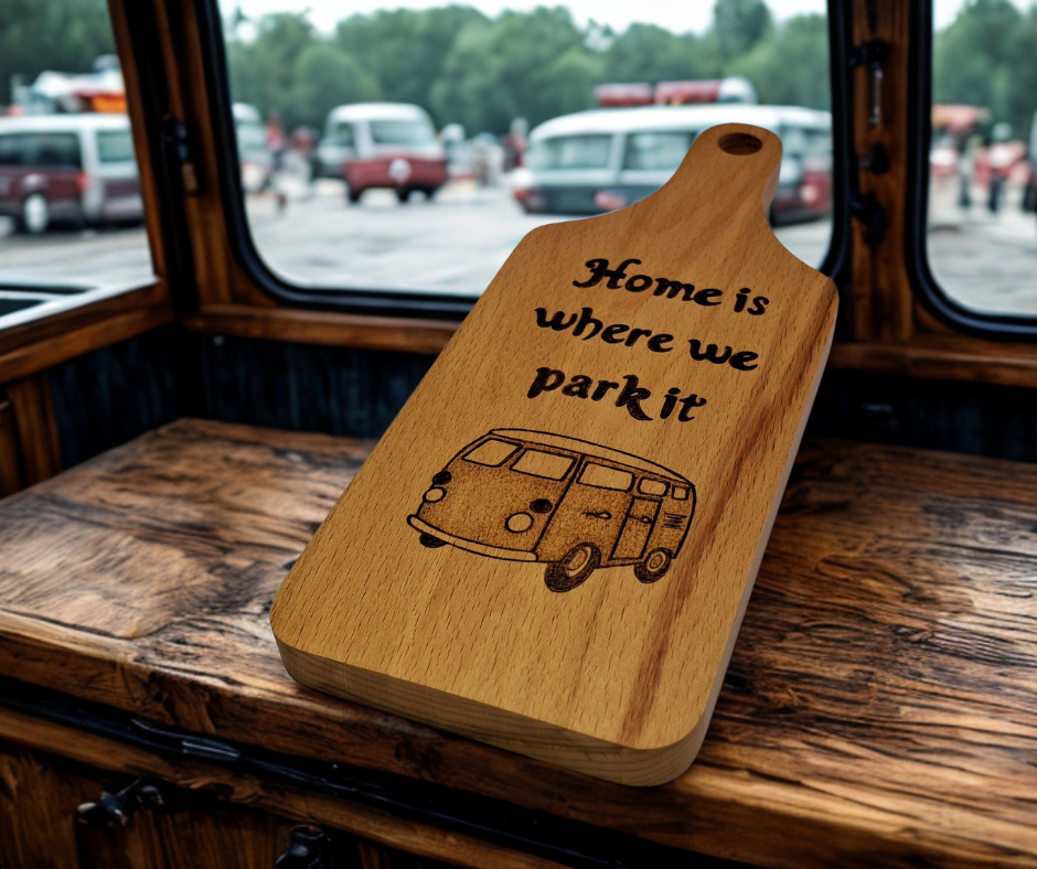 A small, hand-cut beechwood chopping board with hand-decorated pyrography wording "Home Is Where We Park It" and an illustration of a traditional campervan. It's finished with food-safe hardwax oil.
