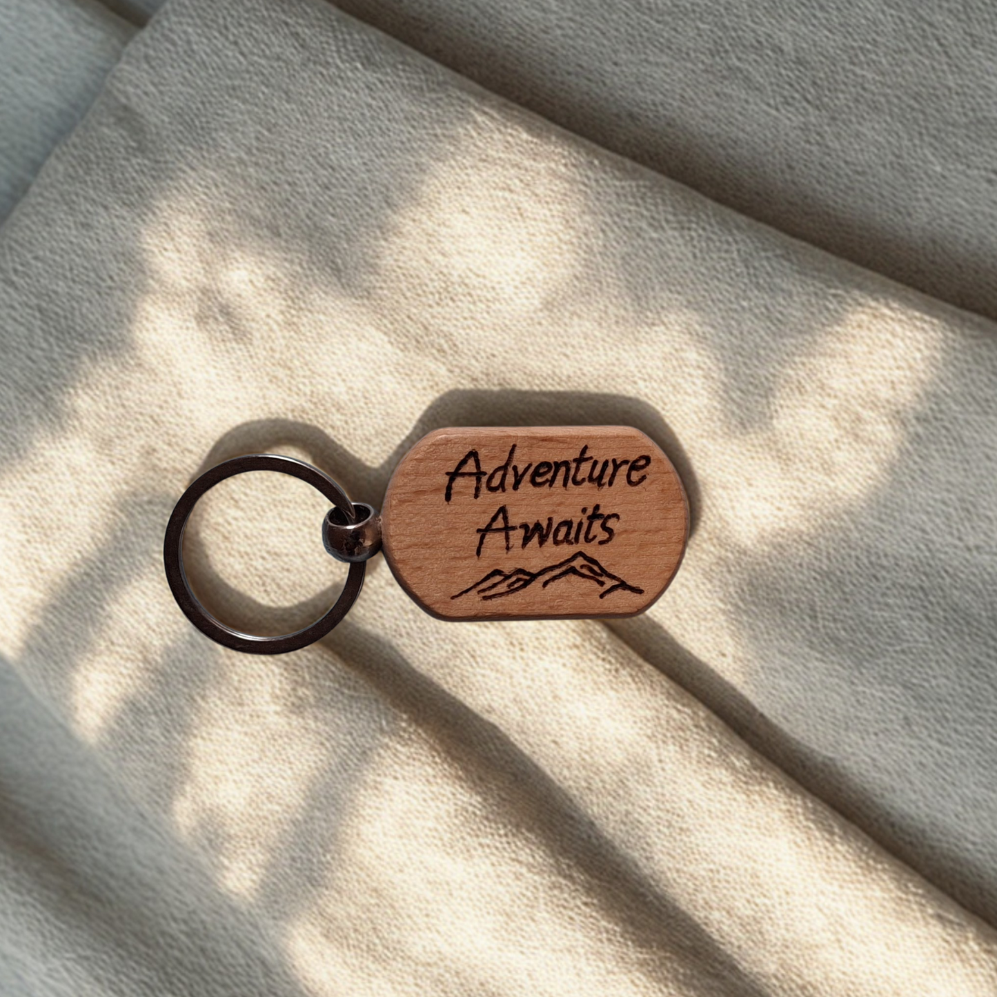 Oval beechwood keyring with 'Adventure Awaits' text and mountain range pyrography design and chrome split ring