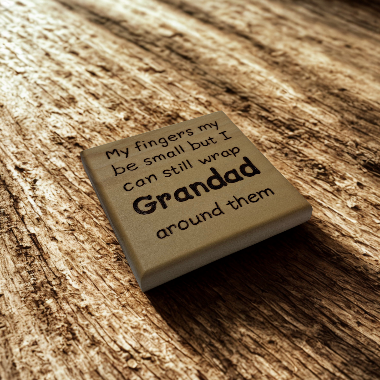 A light wood coaster, square in shape, with pyrography lettering. The text reads: "My fingers my be small but I can still wrap Grandad around them". The word "Grandad" is significantly larger and bolder than the rest of the text.
