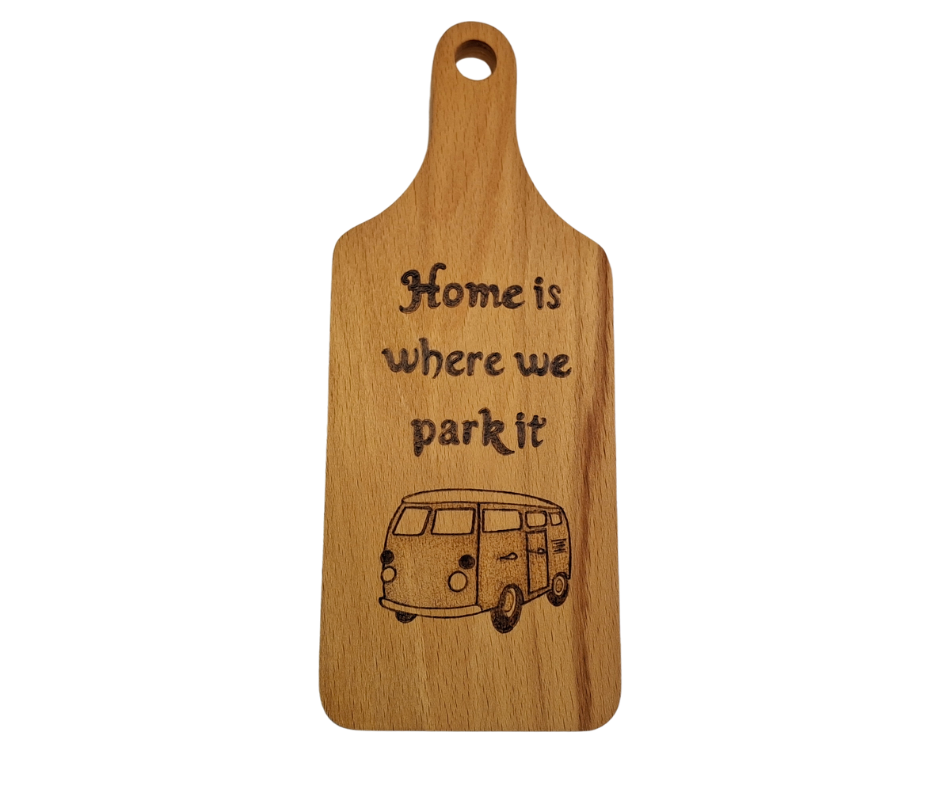A small, hand-cut beechwood chopping board with hand-decorated pyrography wording "Home Is Where We Park It" and an illustration of a traditional campervan. It's finished with food-safe hardwax oil.