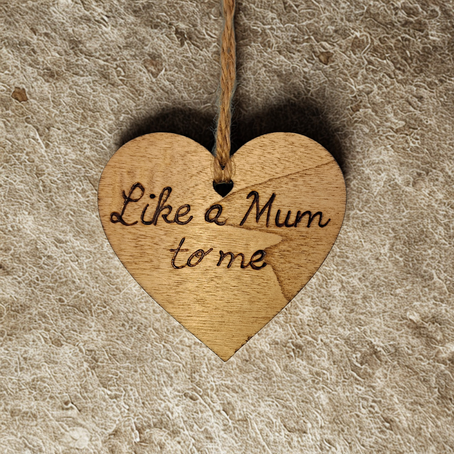 Heart-shaped wooden ornament, hand-drawn with pyrography, featuring the engraved phrase "Like a Mum to me" in a decorative script, set against a textured background.