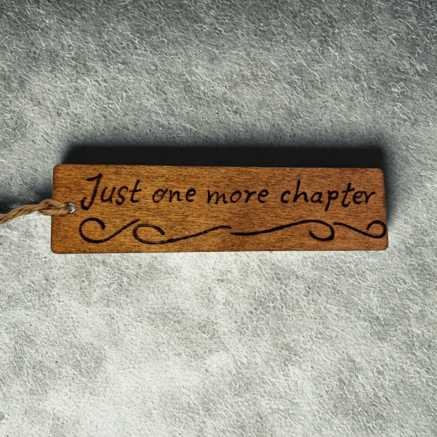 Dark wood bookmark with "Just one more chapter" pyrography and a patterned line illustration.