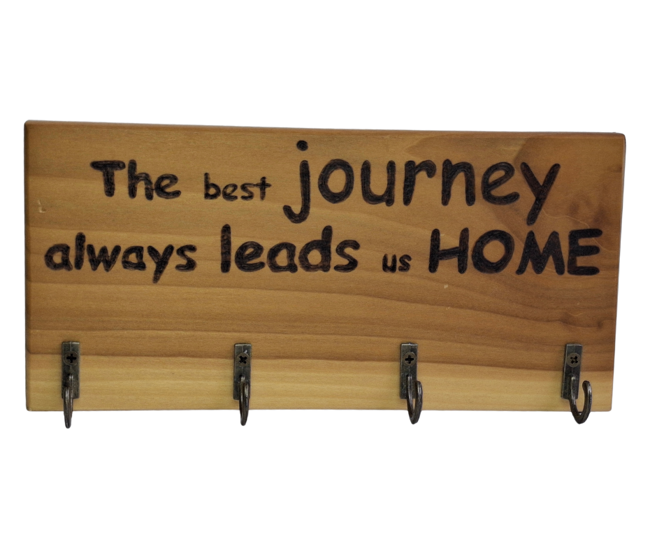 A four-key hook hanger crafted from two-tone Tulipwood, featuring hand-burnt lettering that reads "The best journey always leads us home." The wood has visible grain, showcasing its natural variations.
