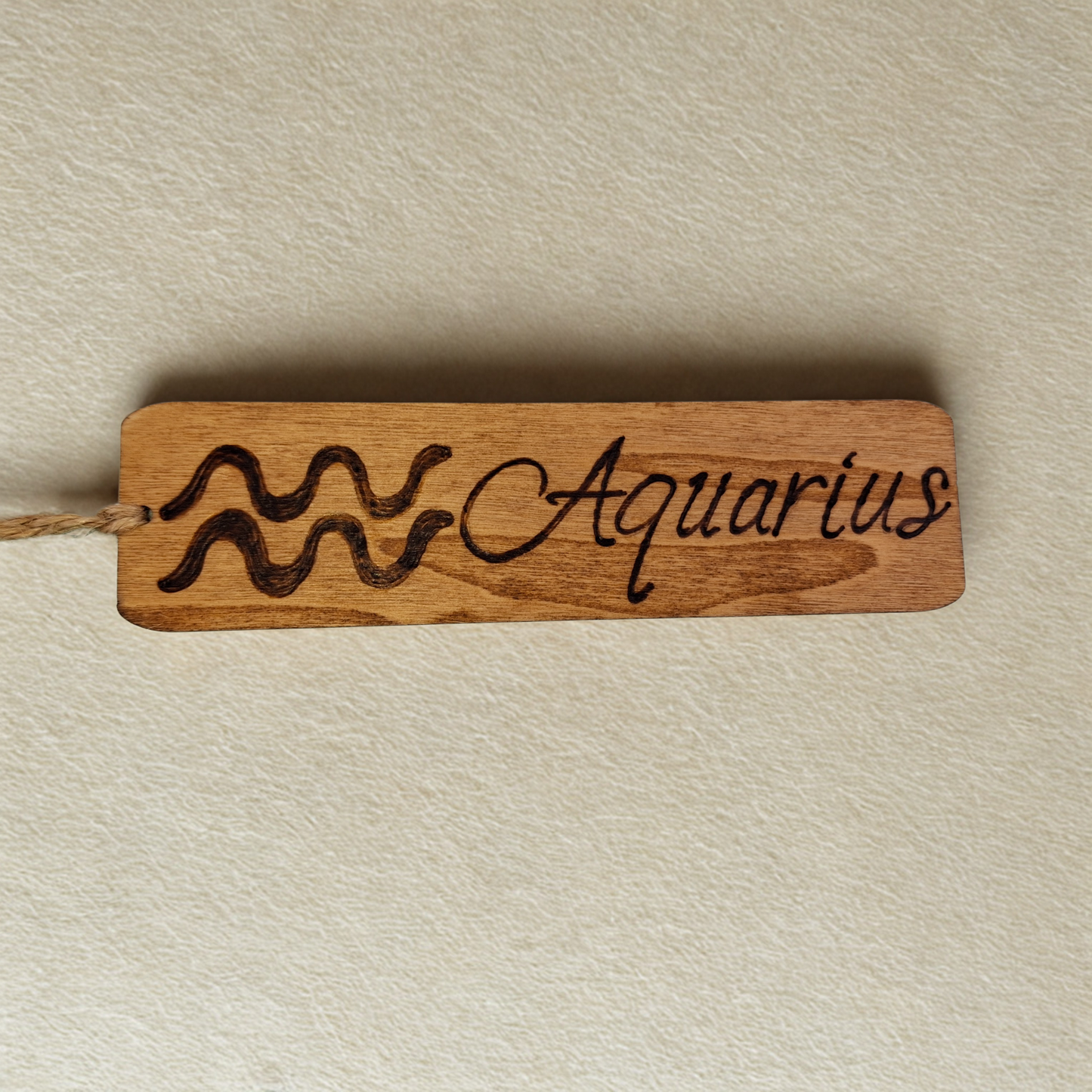 Dark wood bookmark with "Aquarius" pyrography and a star sign illustration.