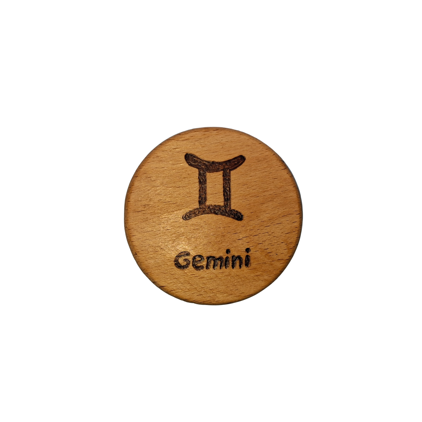 Close-up of a light-colored beechwood circle, 5cm in diameter and 0.4cm thick, featuring the words "Gemini" and an illustration of the star sign symbol, hand-burned into its surface using pyrography. The wood has a smooth, waxed finish and the text is clearly legible.