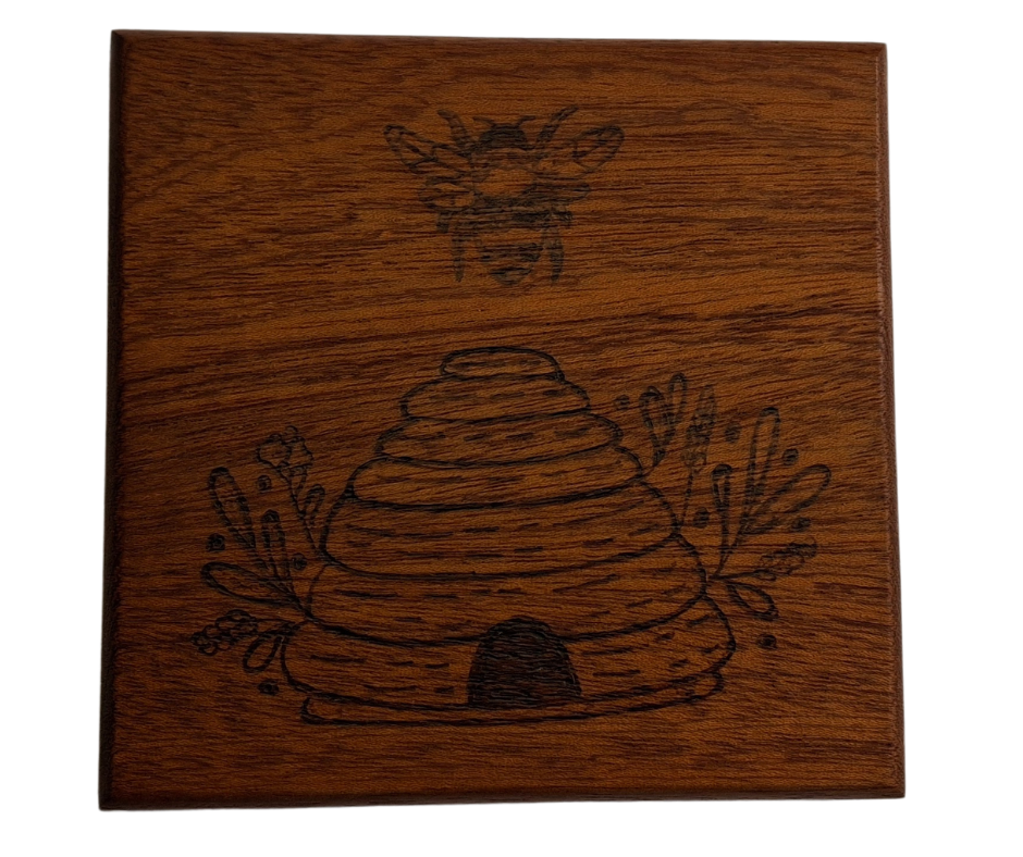 Sapele coaster with chamfered edges with a bee flying over a hive design burnt in