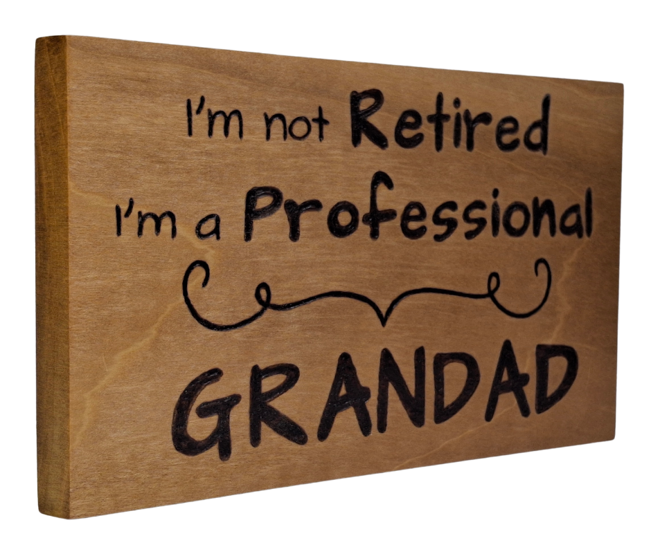 Hand-burnt wooden sign featuring the witty "I'm not retired I'm a professional Grandad" text, separated by a charming pyrography divider.