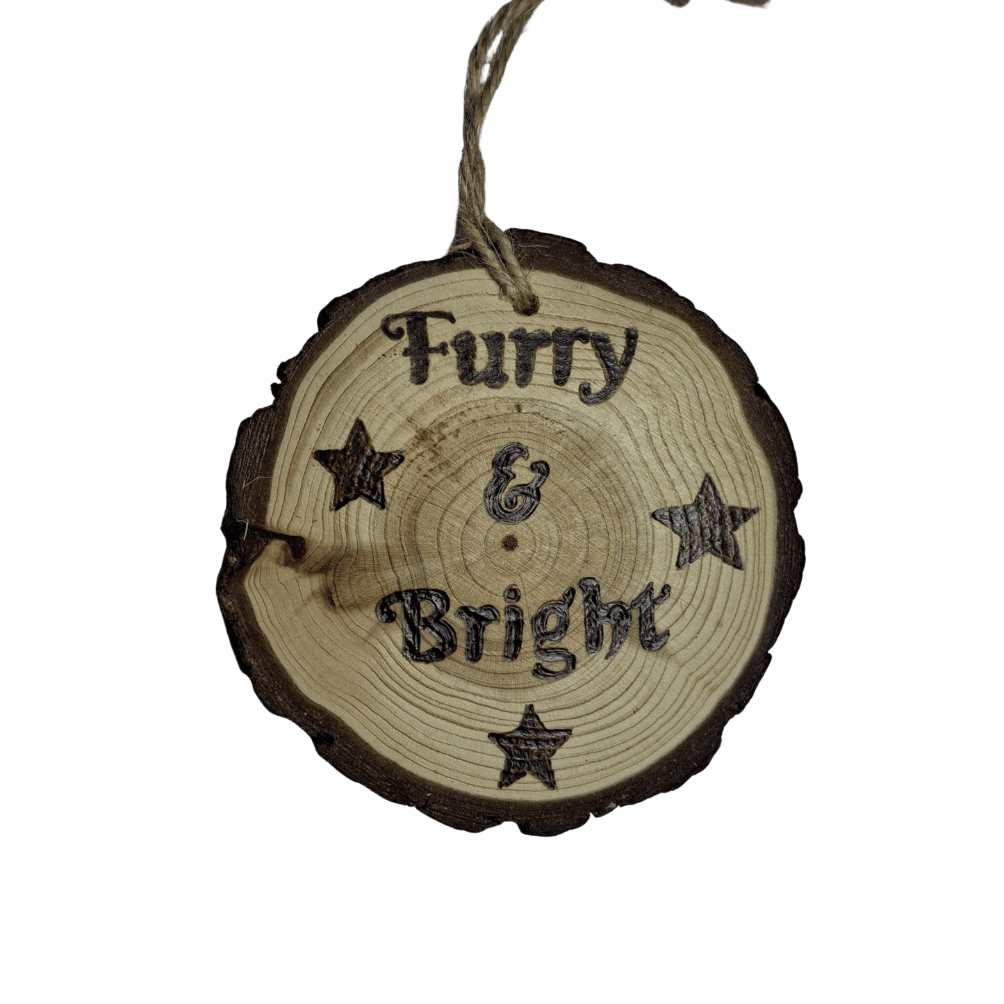 A close-up of a Christmas ornament on a black background. The ornament is a round wooden log slice with a jute rope for hanging. The front of the log slice is decorated with a pyrography design featuring the text "Furry & Bright" surrounded by four stars.