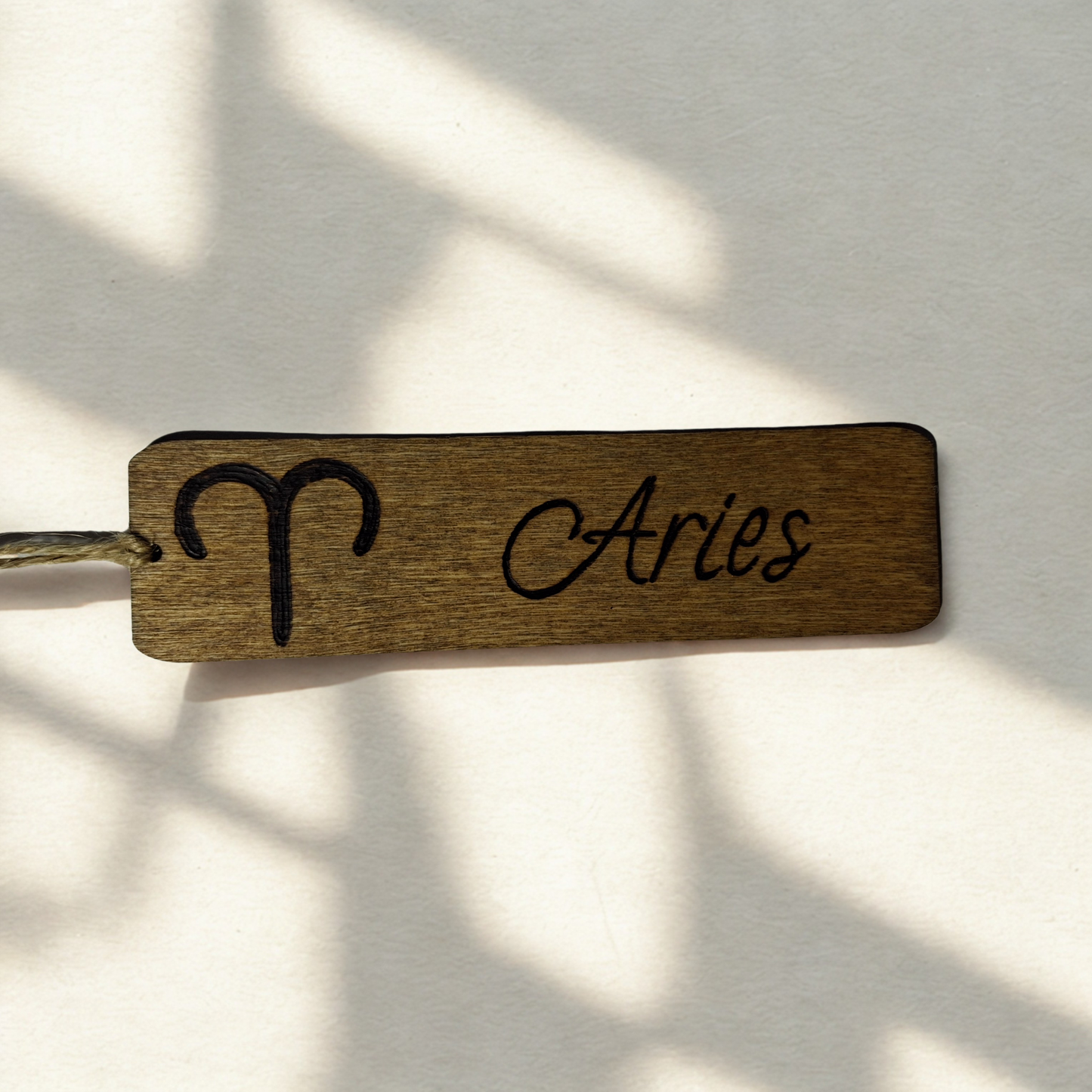 Dark wood bookmark with "Aries" pyrography and a star sign illustration.