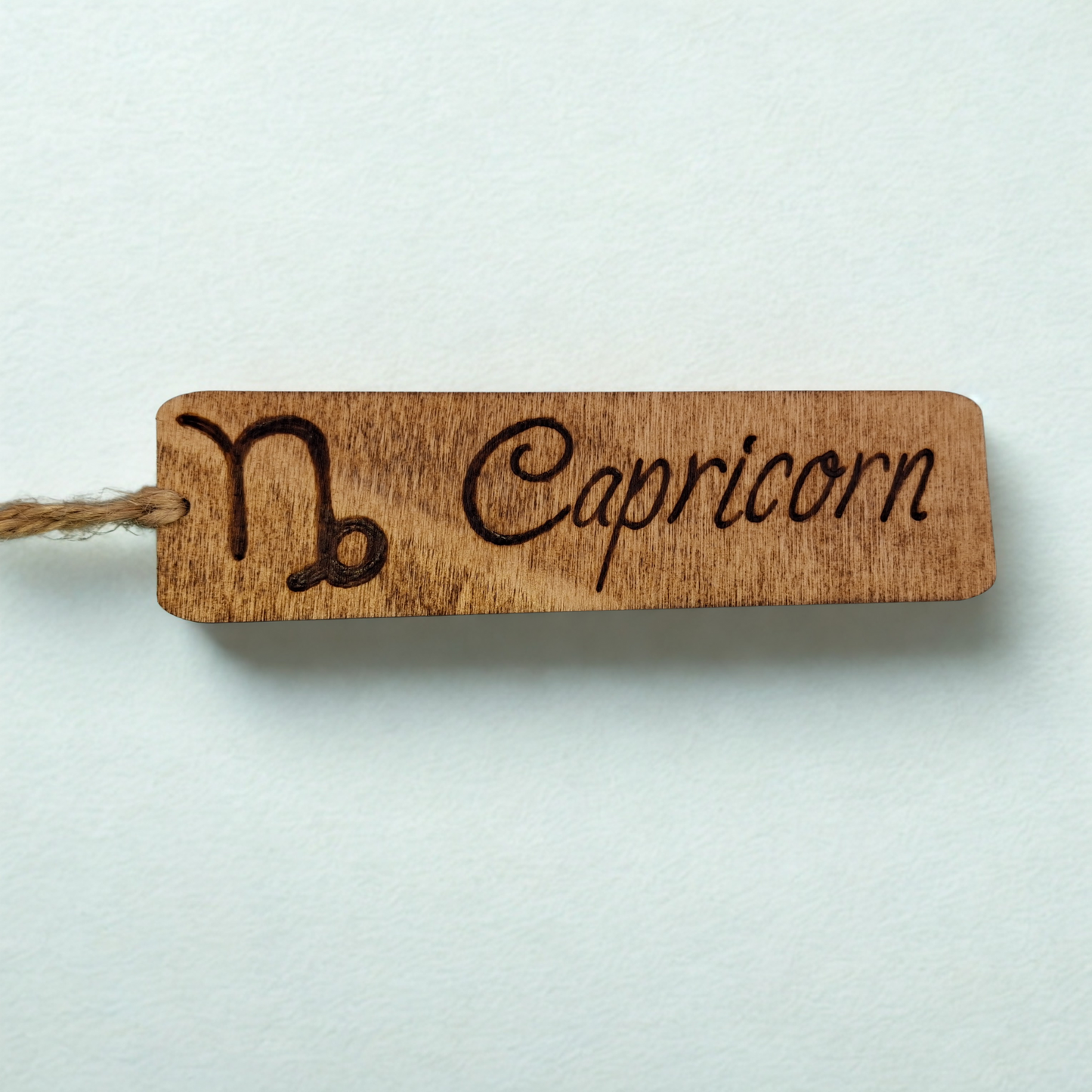 Dark wood bookmark with "Capricorn" pyrography and a star sign illustration.