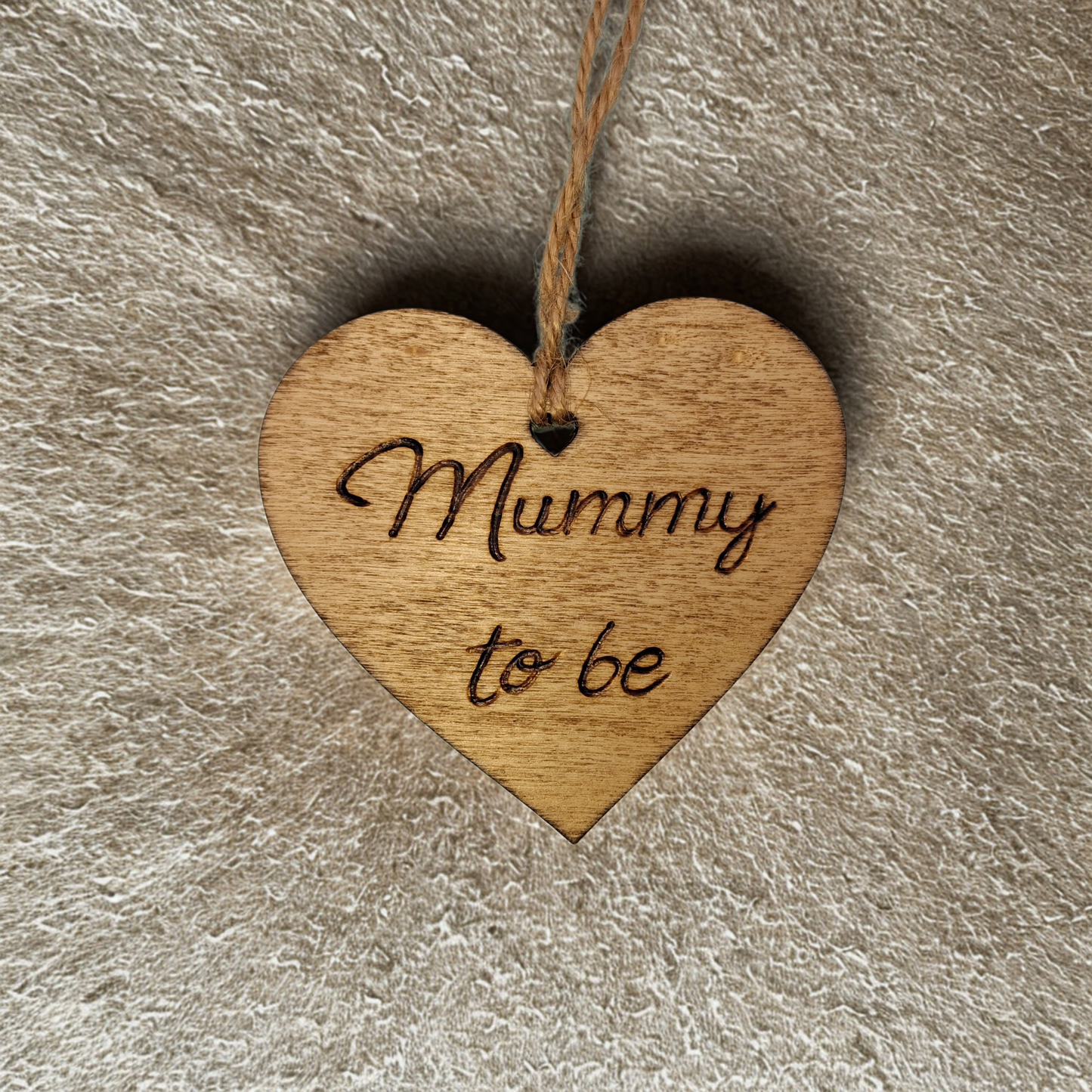 Heart-shaped wooden ornament, hand-drawn with pyrography, featuring the engraved phrase "Mummy to be", set against a textured background.