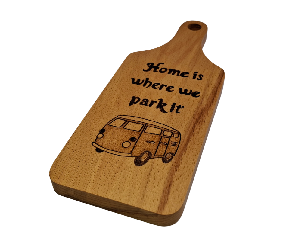 A small, hand-cut beechwood chopping board with hand-decorated pyrography wording "Home Is Where We Park It" and an illustration of a traditional campervan. It's finished with food-safe hardwax oil.
