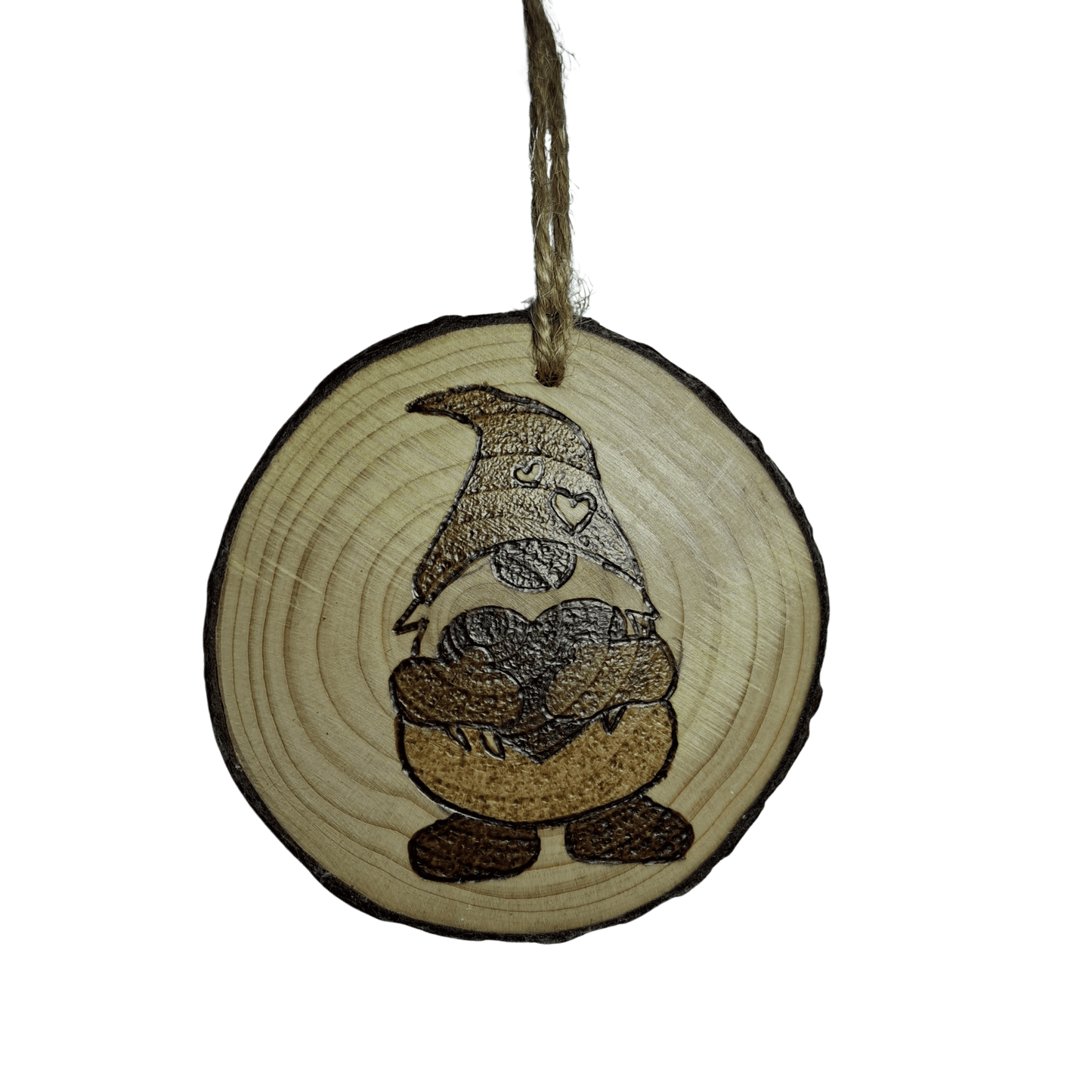 A small Christmas ornament, a wooden log slice with a jute rope for hanging, is shown on a black background. The ornament is decorated with a pyrography design of a gonk holding a heart, with a pattern of smaller hearts on its hat.