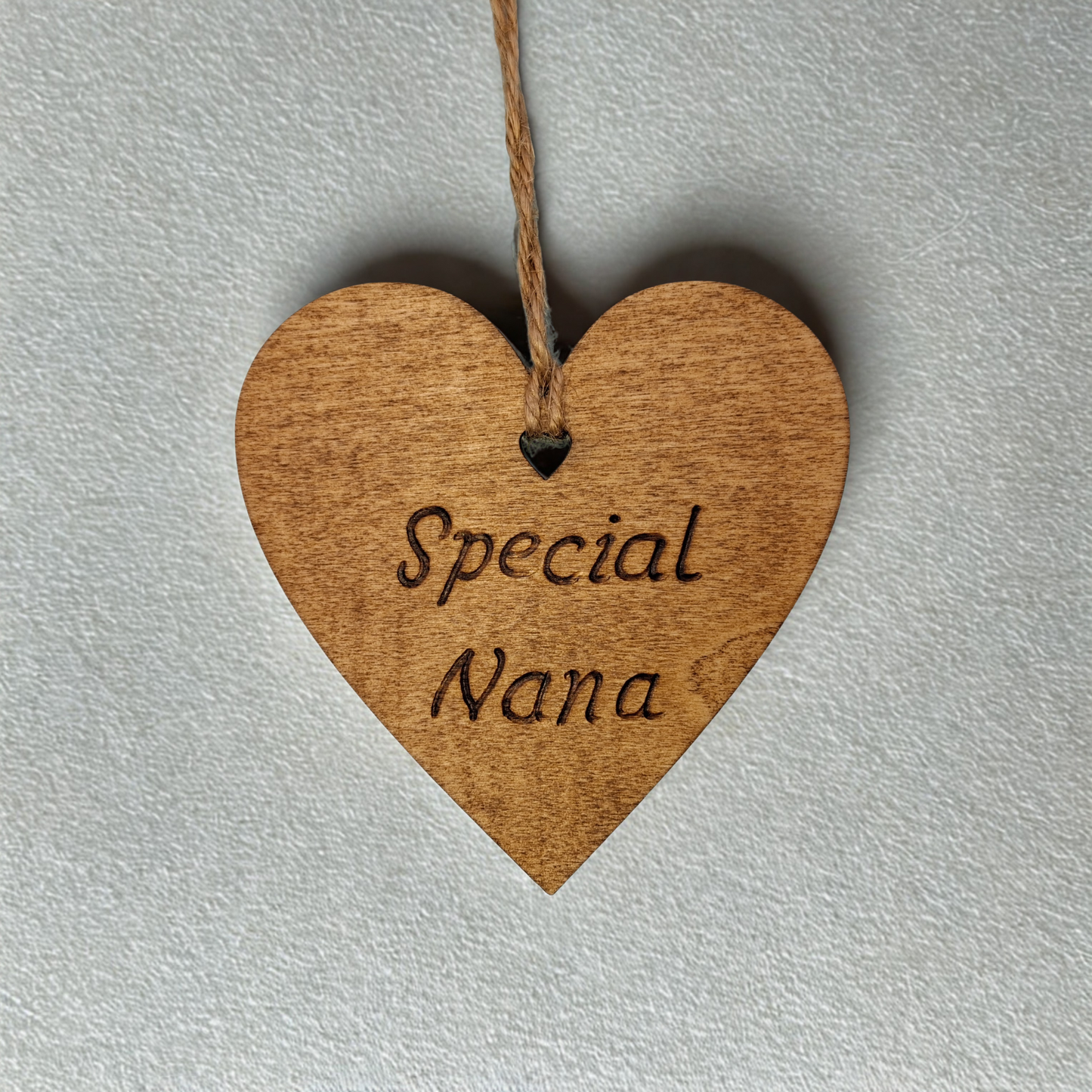 Heart-shaped wooden ornament, hand-drawn with pyrography, featuring the engraved phrase "Special Nana" in a decorative script, set against a textured background.
