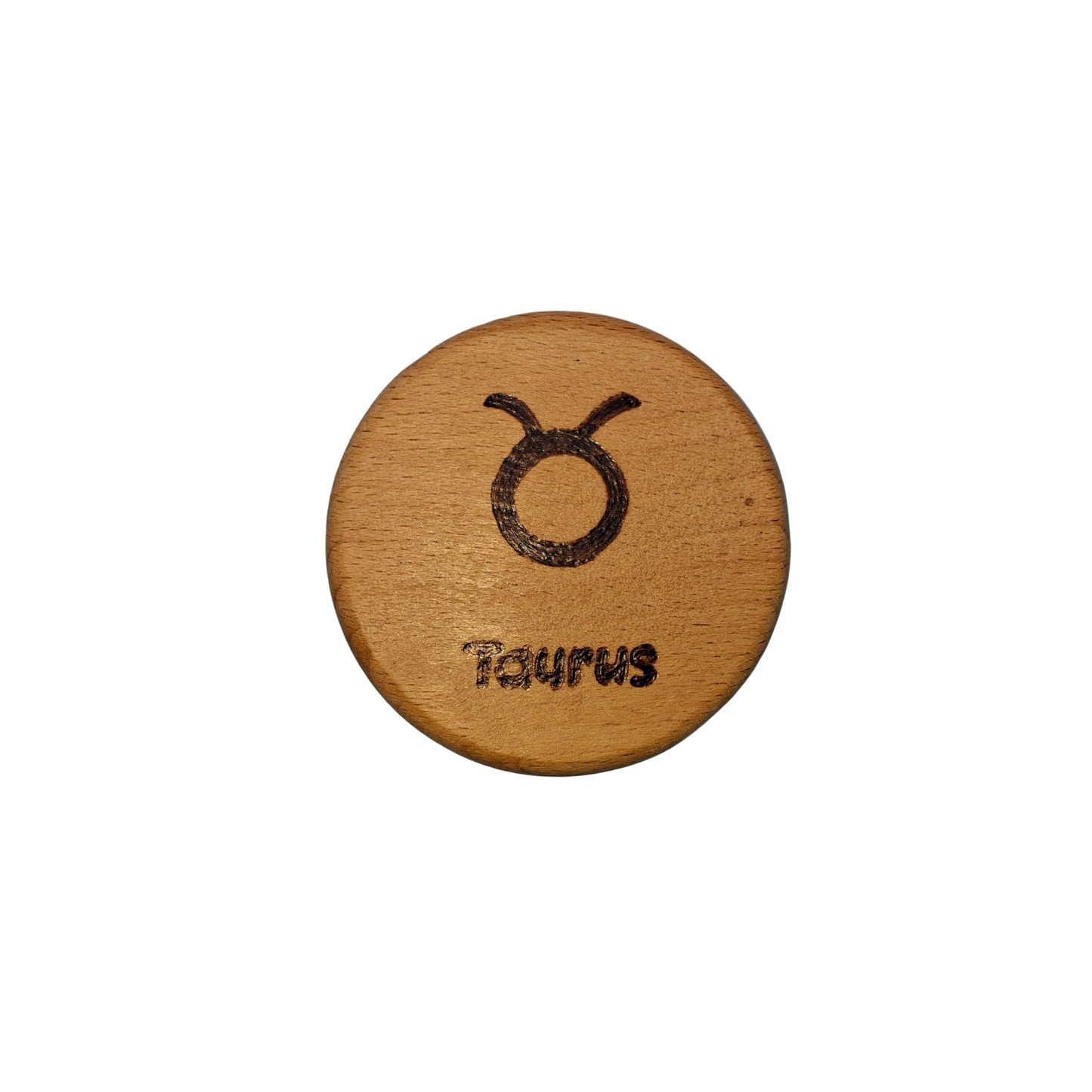 Close-up of a light-colored beechwood circle, 5cm in diameter and 0.4cm thick, featuring the words "Taurus" and an illustration of the star sign symbol, hand-burned into its surface using pyrography. The wood has a smooth, waxed finish and the text is clearly legible.