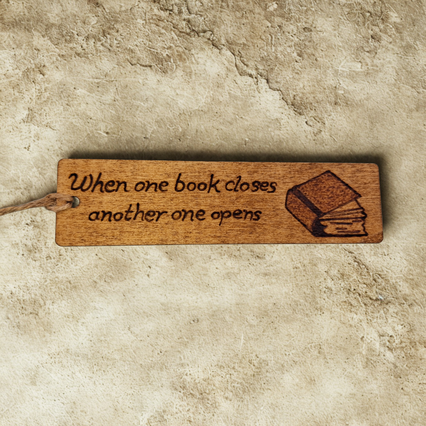 Dark wood bookmark with "When one book closes another one opens" pyrography and a slightly open book illustration.
