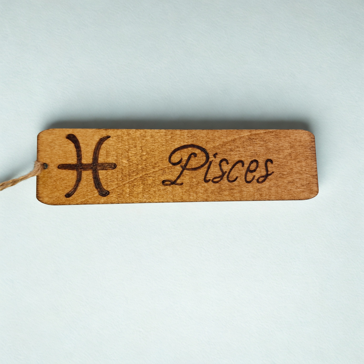 Dark wood bookmark with "Pisces" pyrography and a star sign illustration.