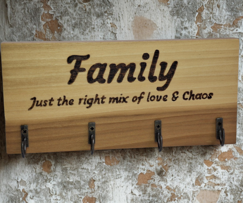 A four-key hook hanger crafted from two-tone Tulipwood, featuring hand-burnt lettering that reads "Family just the mix of love & chaos." The wood has visible grain, showcasing its natural variations.
