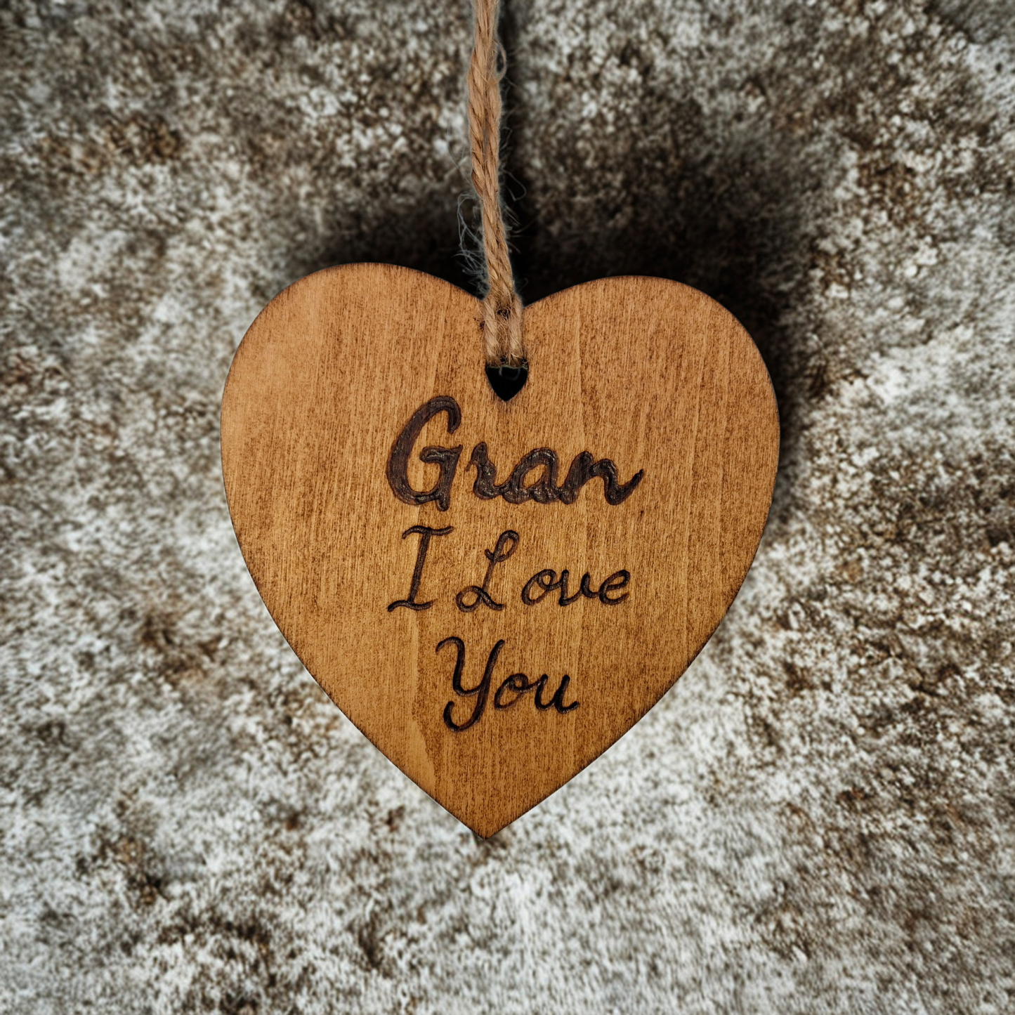 Heart-shaped wooden ornament, hand-drawn with pyrography, featuring the engraved phrase "Gran I Love You" in a decorative script, set against a textured background.