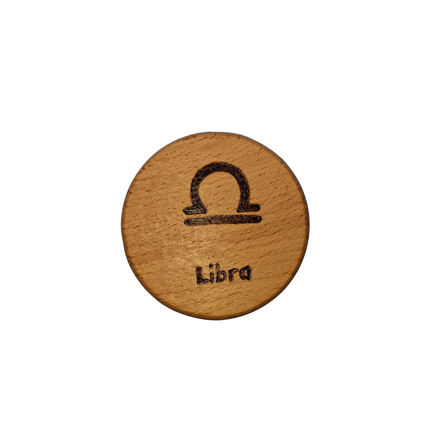 Close-up of a light-colored beechwood circle, 5cm in diameter and 0.4cm thick, featuring the words "Libra" and an illustration of the star sign symbol, hand-burned into its surface using pyrography. The wood has a smooth, waxed finish and the text is clearly legible.