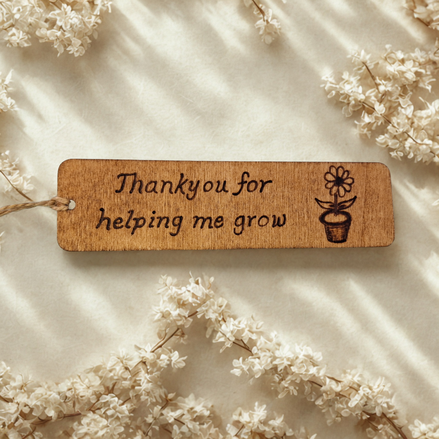 Dark wood bookmark with "Thankyou for helping me grow" pyrography and a flower in a pot illustration.