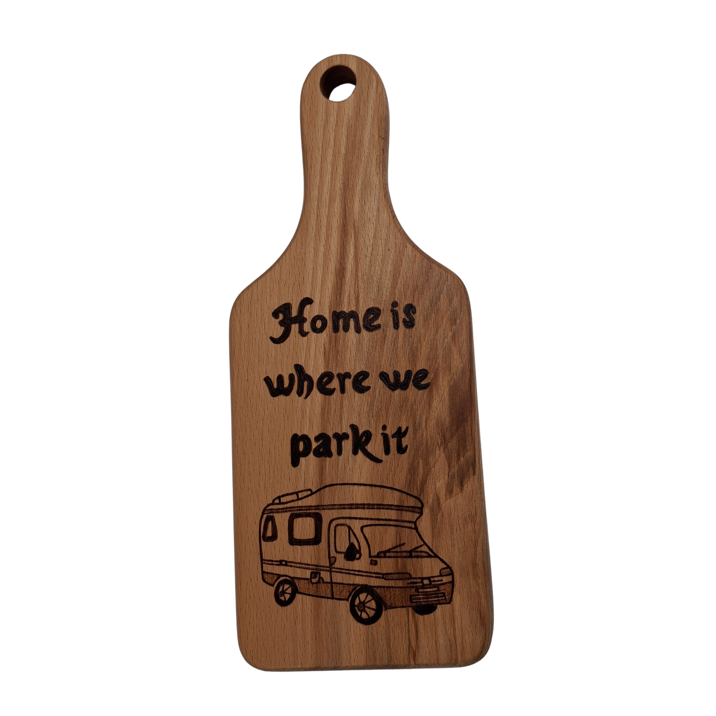 Wooden cutting board with hand burnt text "Home is where we park it" text and camper illustration on a clear background