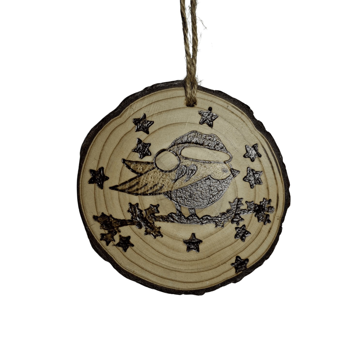 A Christmas ornament, made from a wooden log slice with a jute rope for hanging, is shown on a black background. The front of the ornament is decorated with a pyrography design of a sleeping bird wearing a Christmas hat and surrounded by stars.