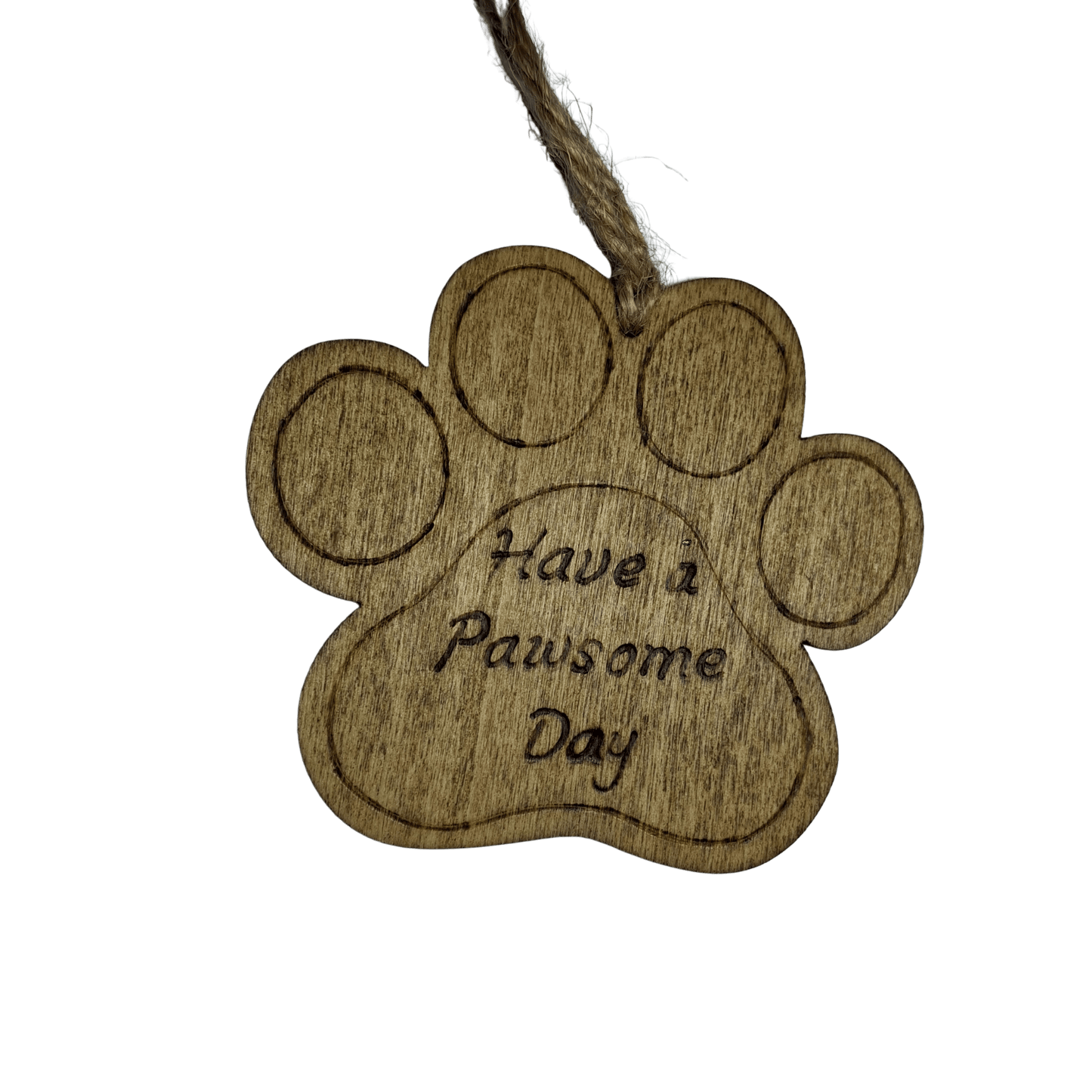 A light brown, wooden, paw-print-shaped ornament. It has a hole at the top with a piece of natural twine for hanging. The words "Have a Pawsome Day" are hand burnt in a cursive font into the center of the paw. The background is solid black.