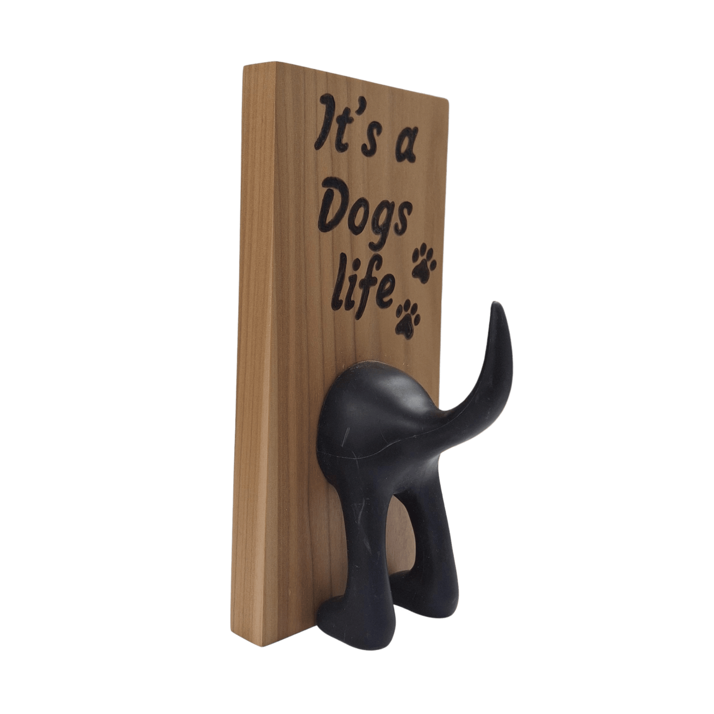 A vertical wooden wall plaque featuring the hand-burnt with pyrography text "It's a Dogs life" in a black, casual script. To the right of the word "life" are three small paw prints. A black, molded figure of a dog's rear end is attached below the text, with the upturned tail forming a hook.