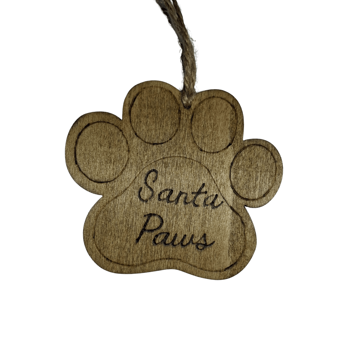 A light brown wooden decoration in the shape of a dog's paw print. A piece of natural twine is threaded through a hole at the top for hanging. The words "Santa Paws" are carved in a cursive font into the center of the paw. The background is solid black.