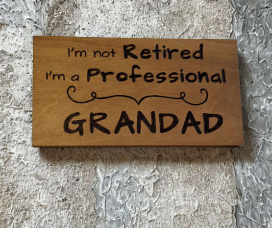 Wooden plaque hand-decorated with "I'm not retired I'm a professional Grandad" pyrography and a decorative divider.