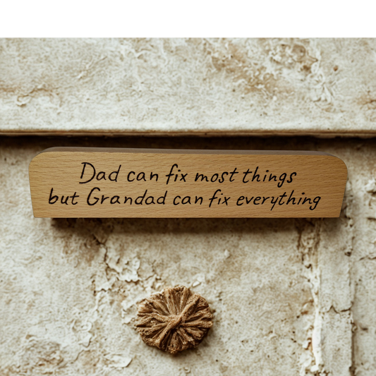 A long, narrow piece of light wood, rounded at the top and bottom edges  a desk plaque or sign. It features pyrography text that reads: "Dad can fix most things but Grandad can fix everything."