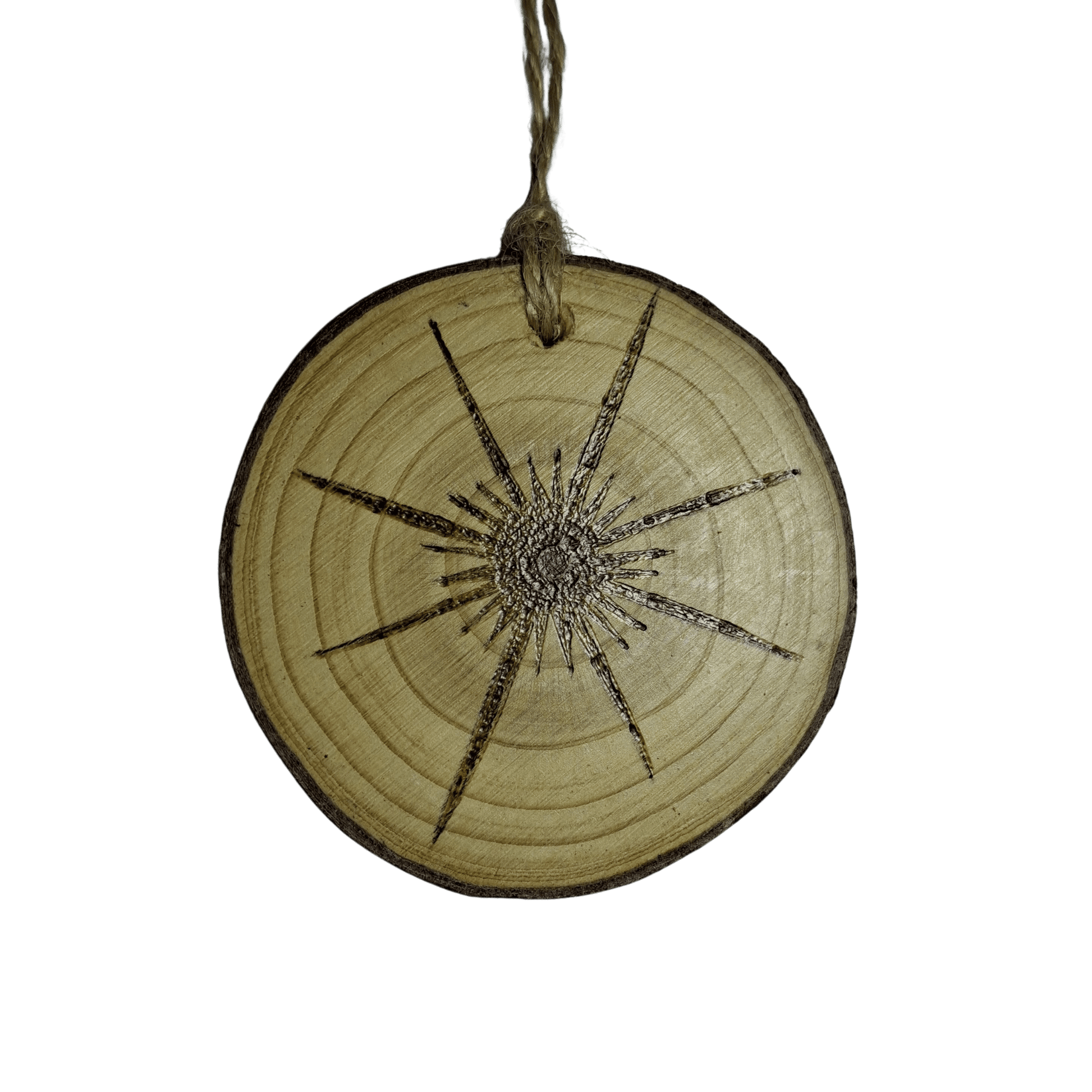 
A small Christmas ornament, a wooden log slice with a jute rope for hanging, is centered against a black background. The ornament is decorated with a detailed pyrography design of an eight-pointed star, with rays extending outwards.