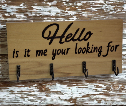 A four-hook hanger crafted from two-tone Tulipwood, featuring hand-burnt lettering that reads "Hello, Is It Me You're Looking For?" The wood has visible grain, showcasing its natural variations.