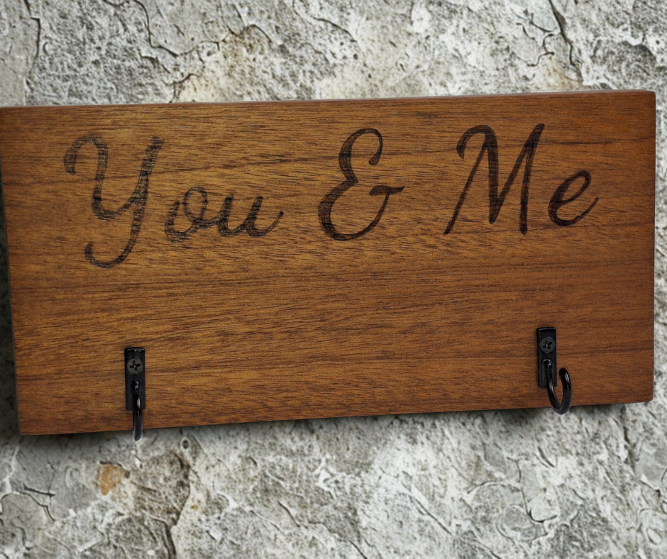 A dark sapele wood 2-hook key hanger with hand-decorated pyrography wording "You & Me".
