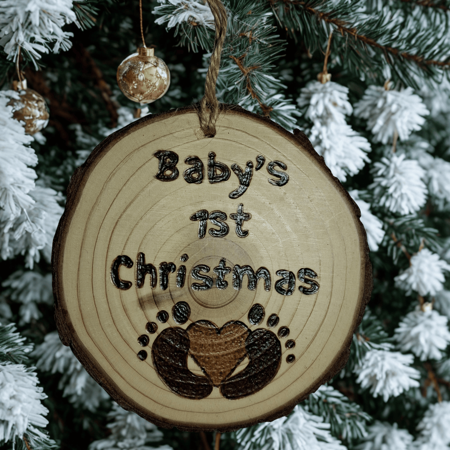 Wooden ornament with 'Baby's 1st Christmas' text and footprints on a Christmas tree background.