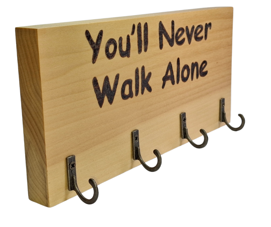 A four-hook hanger crafted from two-tone Tulipwood, featuring hand-burnt lettering that reads "You'll Never Walk Alone." The wood has visible grain, showcasing its natural variations.