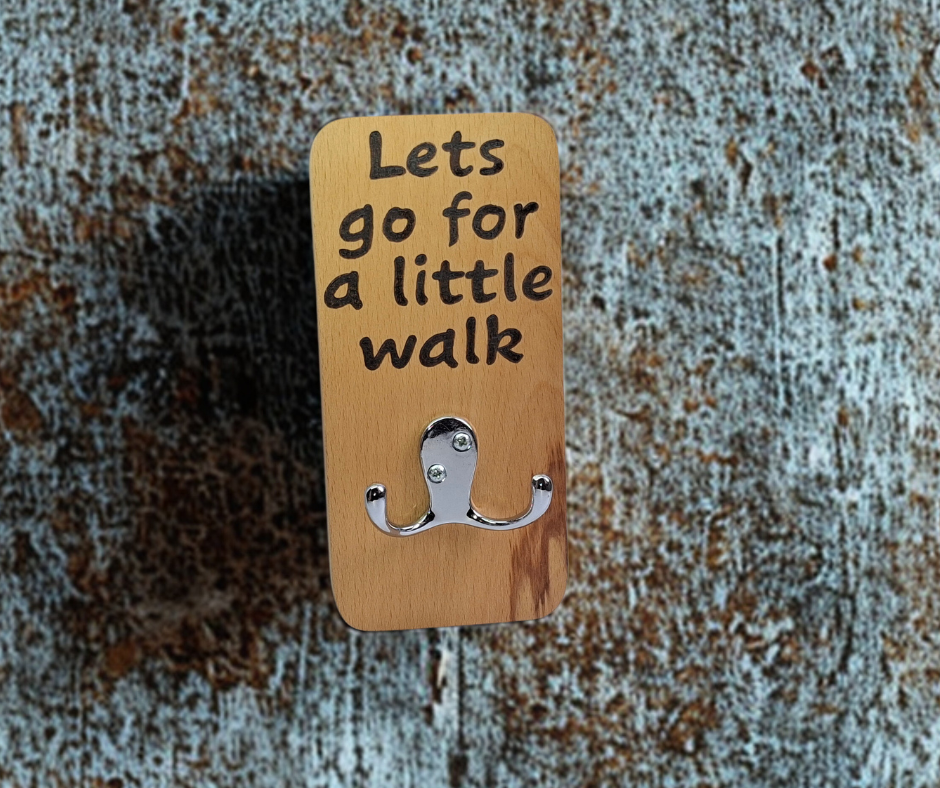 A hand-cut beechwood lead hanger with a double chrome hook for hanging leads. It's decorated with pyrography wording "Let's go for a little walk" and finished with hardwax oil.