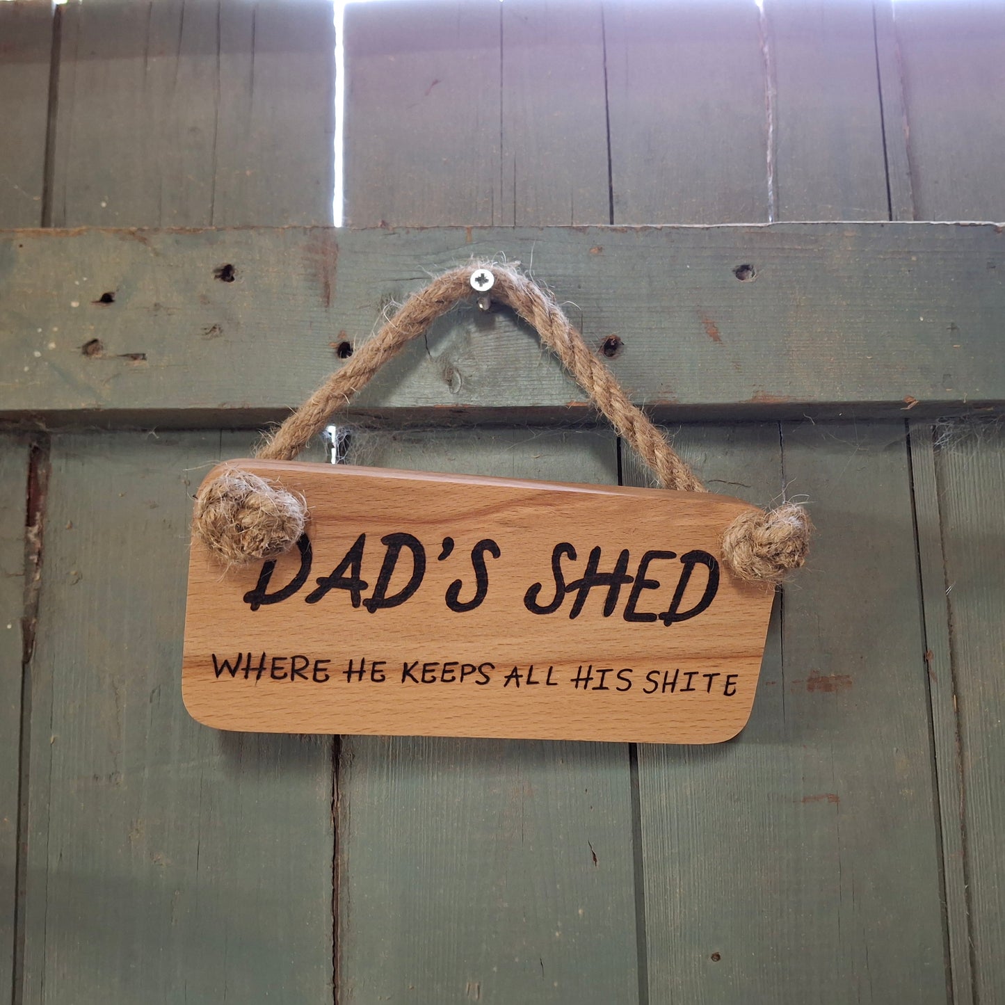 Wooden sign with 'DAD'S SHED' text hanging on a wooden door.