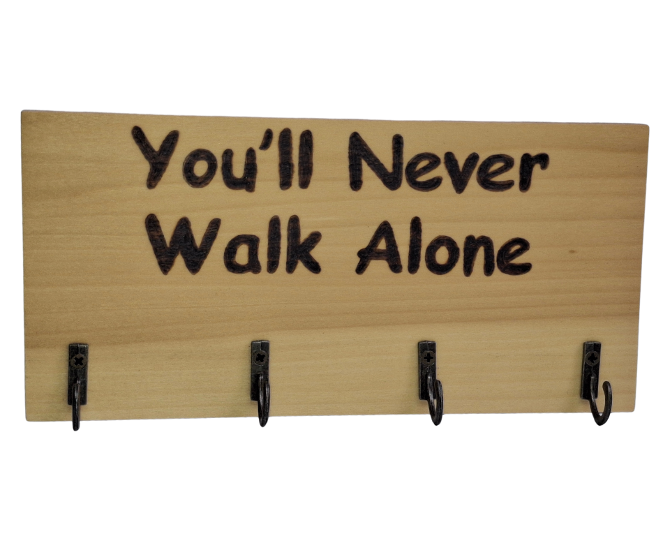 A four-hook hanger crafted from two-tone Tulipwood, featuring hand-burnt lettering that reads "You'll Never Walk Alone." The wood has visible grain, showcasing its natural variations.