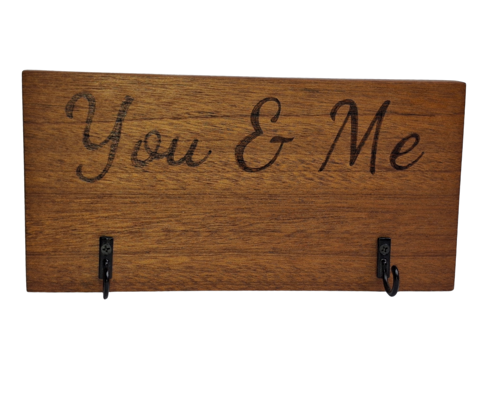 A dark sapele wood 2-hook key hanger with hand-decorated pyrography wording "You & Me".