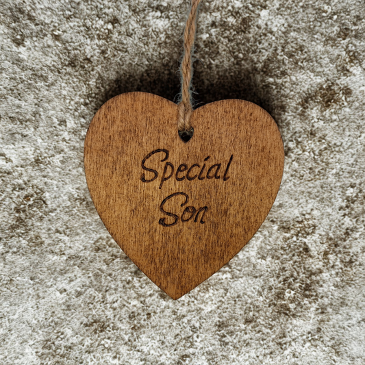 A small, possibly 8cm by 8cm, light-colored wooden heart, decorated with "Special Son" hand-burned into its surface using pyrography. A short length of natural jute rope is tied through the top for hanging.