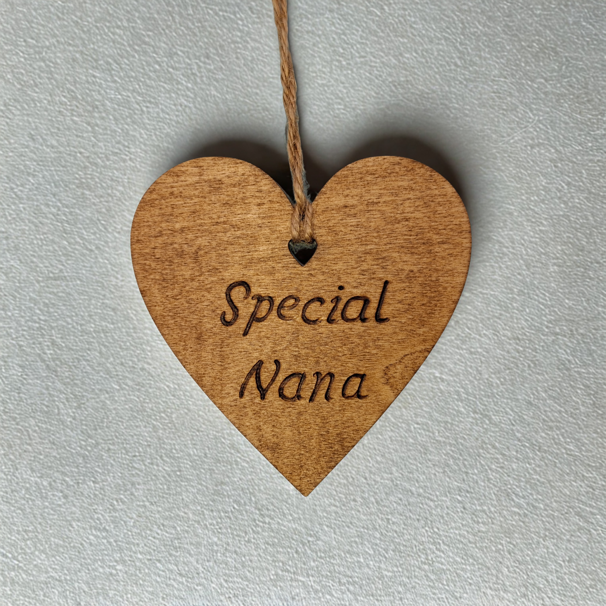 Heart-shaped wooden ornament, hand-drawn with pyrography, featuring the engraved phrase "Special Nana" in a decorative script, set against a textured background.