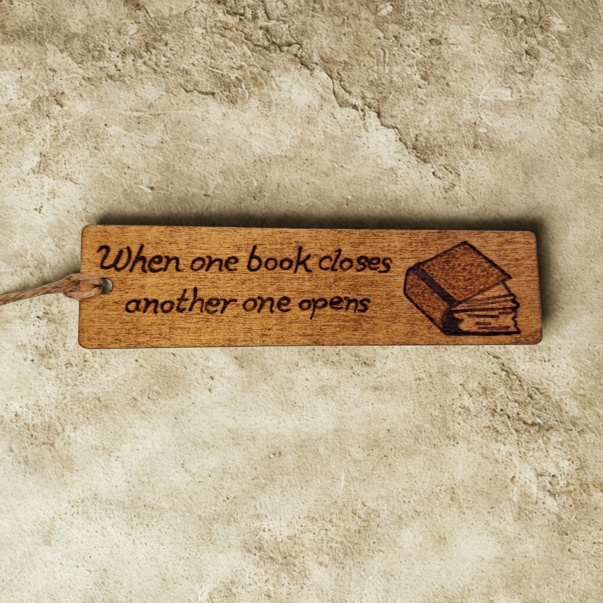 Dark wood bookmark with "When one book closes another one opens" pyrography and a slightly open book illustration.