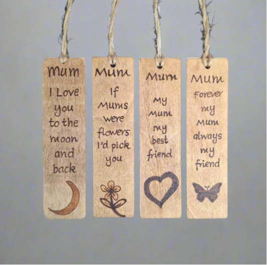 A vertical stack of five light-brown wooden bookmarks, each with a rounded rectangular shape and a piece of natural twine attached through a hole on the left. Each bookmark features dark pyrography (wood-burning) with the text "Best" followed by a family title and a unique accompanying image. From top to bottom, they read: "Best Mum" with an ornate heart, "Best Mummy" with a teddy bear, "Best Grandma" with a stylized flower, "Best Gran" with a tall, slender flower, and "Best Nana" with a leafy branch design